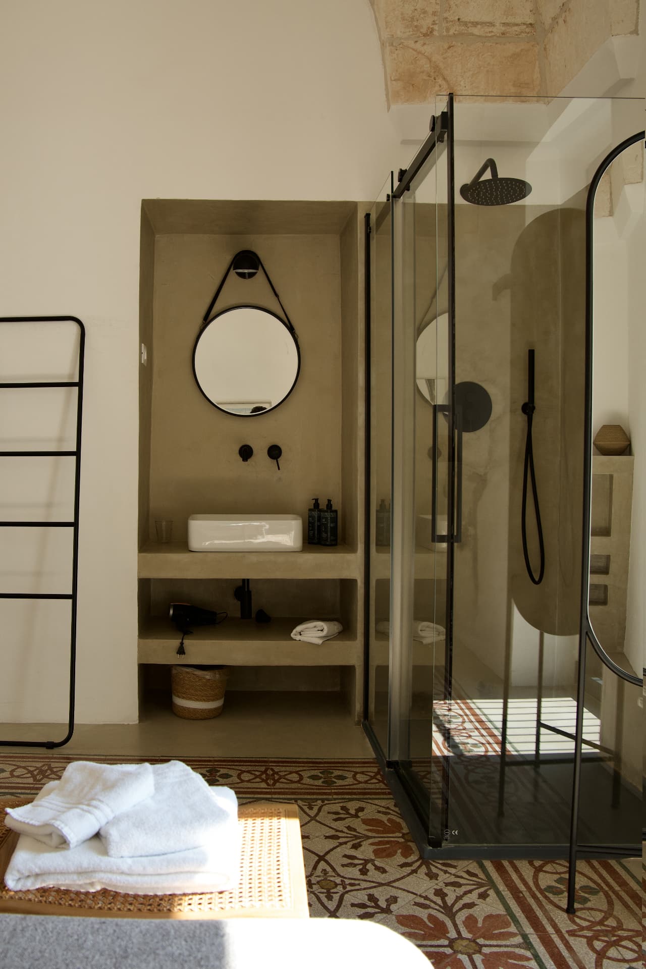 A serene bathroom with black fixtures, a round mirror and a glass shower in a historic Puglian townhouse